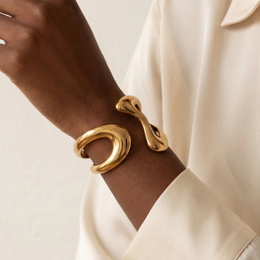 Close up of woman with dark skin wearing gold Pythia cuff bracelet with sculptural fluid design.
