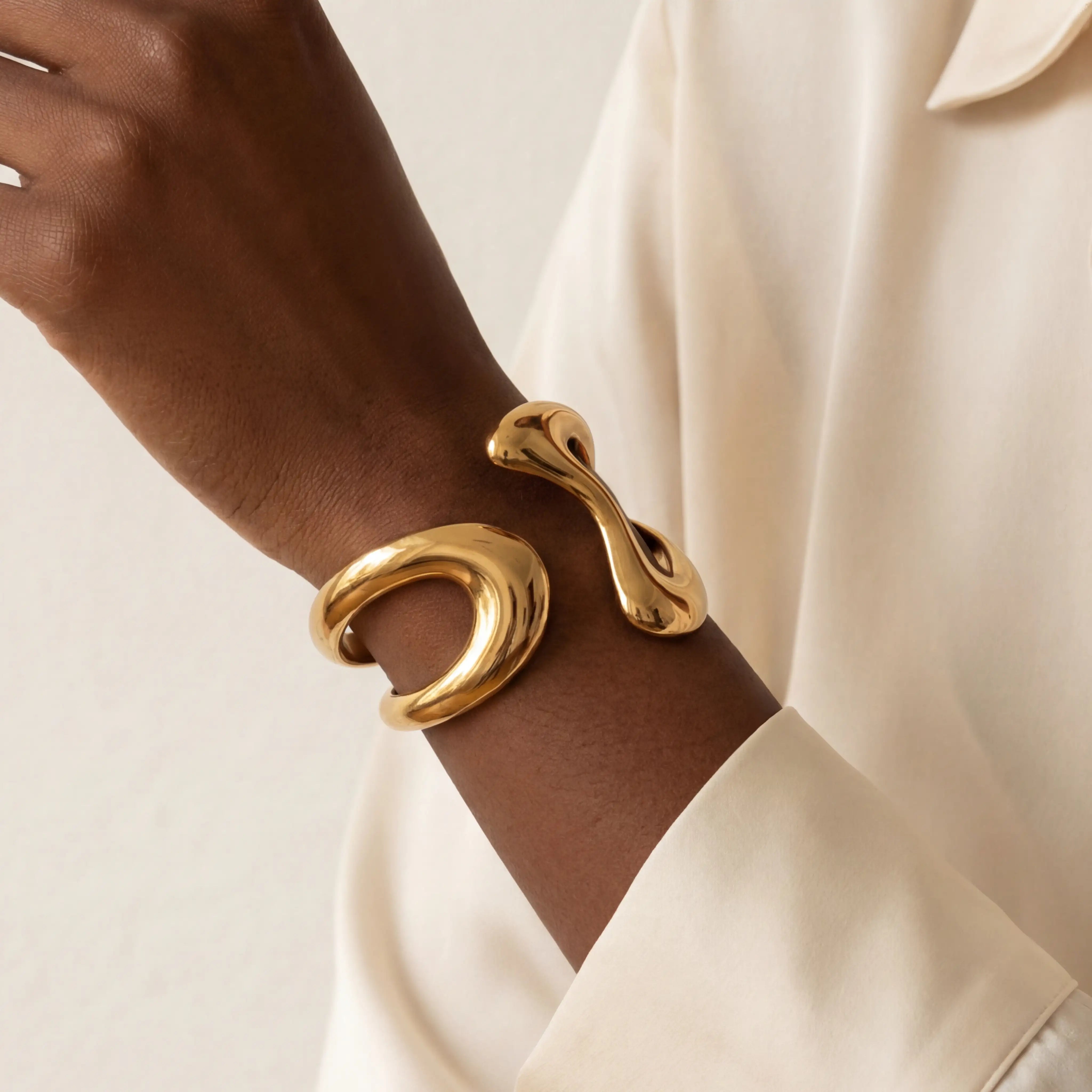 Close up of woman with dark skin wearing gold Pythia cuff bracelet with sculptural fluid design. Main image