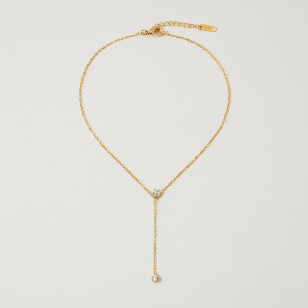 A detailed studio shot of The Reine Necklace by Luminova, showcasing the delicate gold Y-necklace with its sparkling crystal crown and single crystal drop.