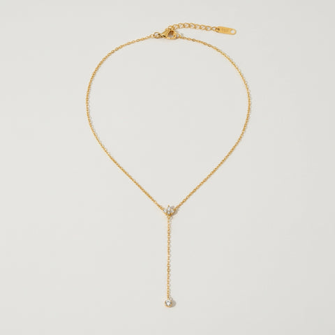 A detailed studio shot of The Reine Necklace by Luminova, showcasing the delicate gold Y-necklace with its sparkling crystal crown and single crystal drop.