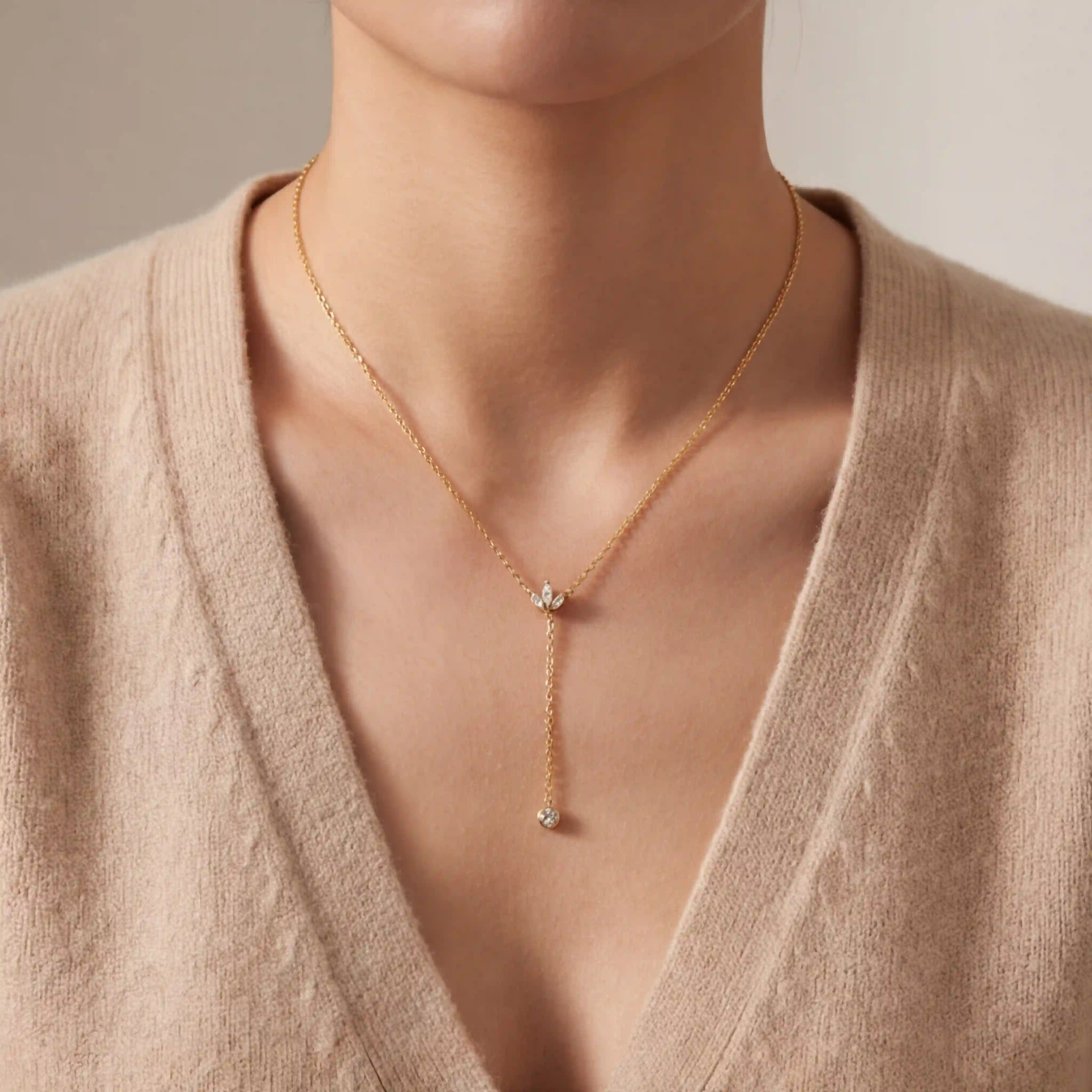 Close up of woman wearing gold Reine Y-necklace with pearl drop on V-neck sweater. Main image