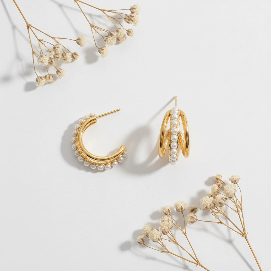 A detailed studio shot of The Siren Hoops by Luminova, showcasing the layered, triple-band design with a central row of pearls, styled with dried flowers.