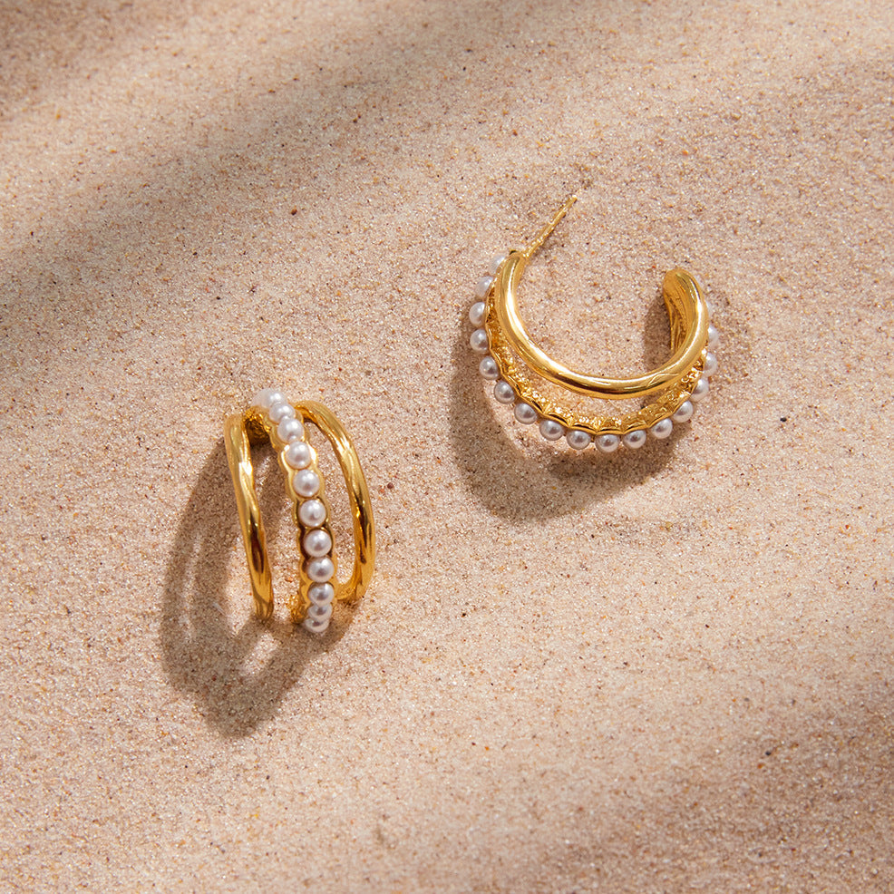The Siren Hoops resting on a bed of fine sand in the sunlight, embodying the perfect waterproof accessory for a luxurious beach vacation.