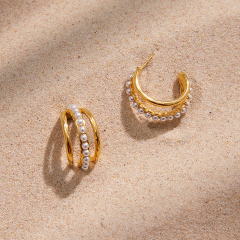 The Siren Hoops resting on a bed of fine sand in the sunlight, embodying the perfect waterproof accessory for a luxurious beach vacation.