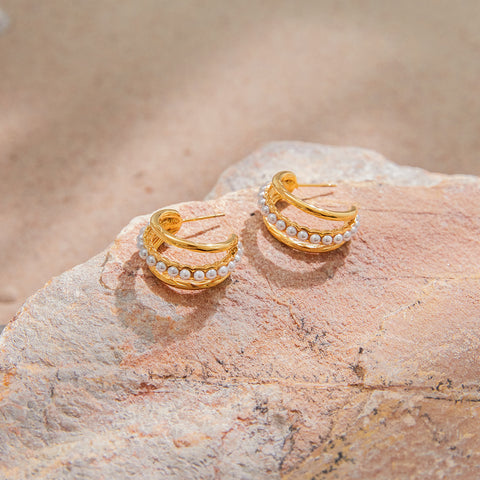 The Siren pearl and gold hoops styled on a natural, rough stone, creating a beautiful contrast between the raw and the refined.