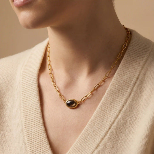 Close up of woman wearing gold Terra necklace with dark oval gemstone pendant vintage style.