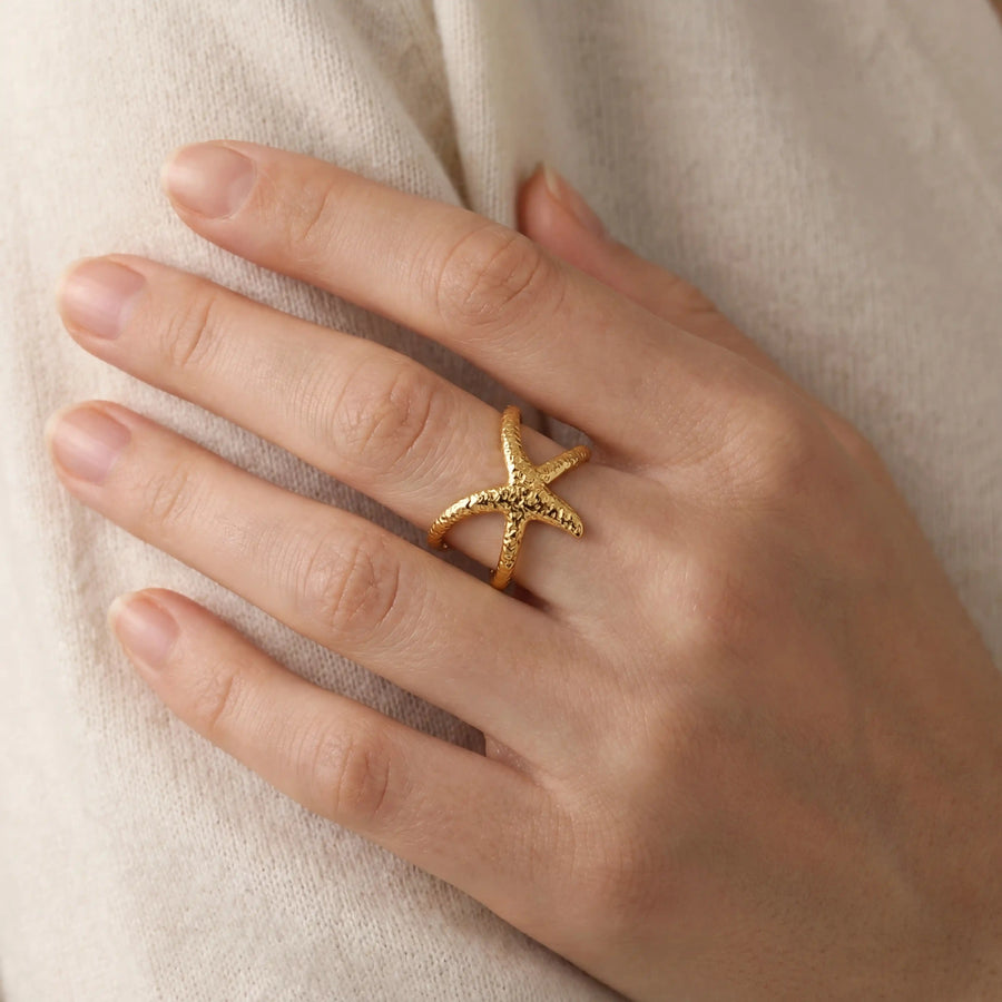 Close up of woman wearing textured gold starfish wrap ring dainty style on ring finger.