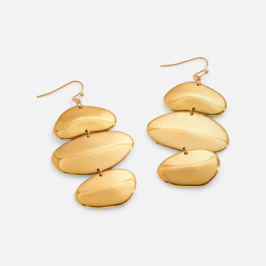 A detailed studio shot of The Thalia Earrings by Luminova, showcasing the cascading design of three organic, polished gold discs, styled with delicate dried flowers.