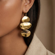 A close-up of a model wearing The Thalia Earrings with a white turtleneck, highlighting their bold scale and how the sculptural gold tiers drop elegantly.