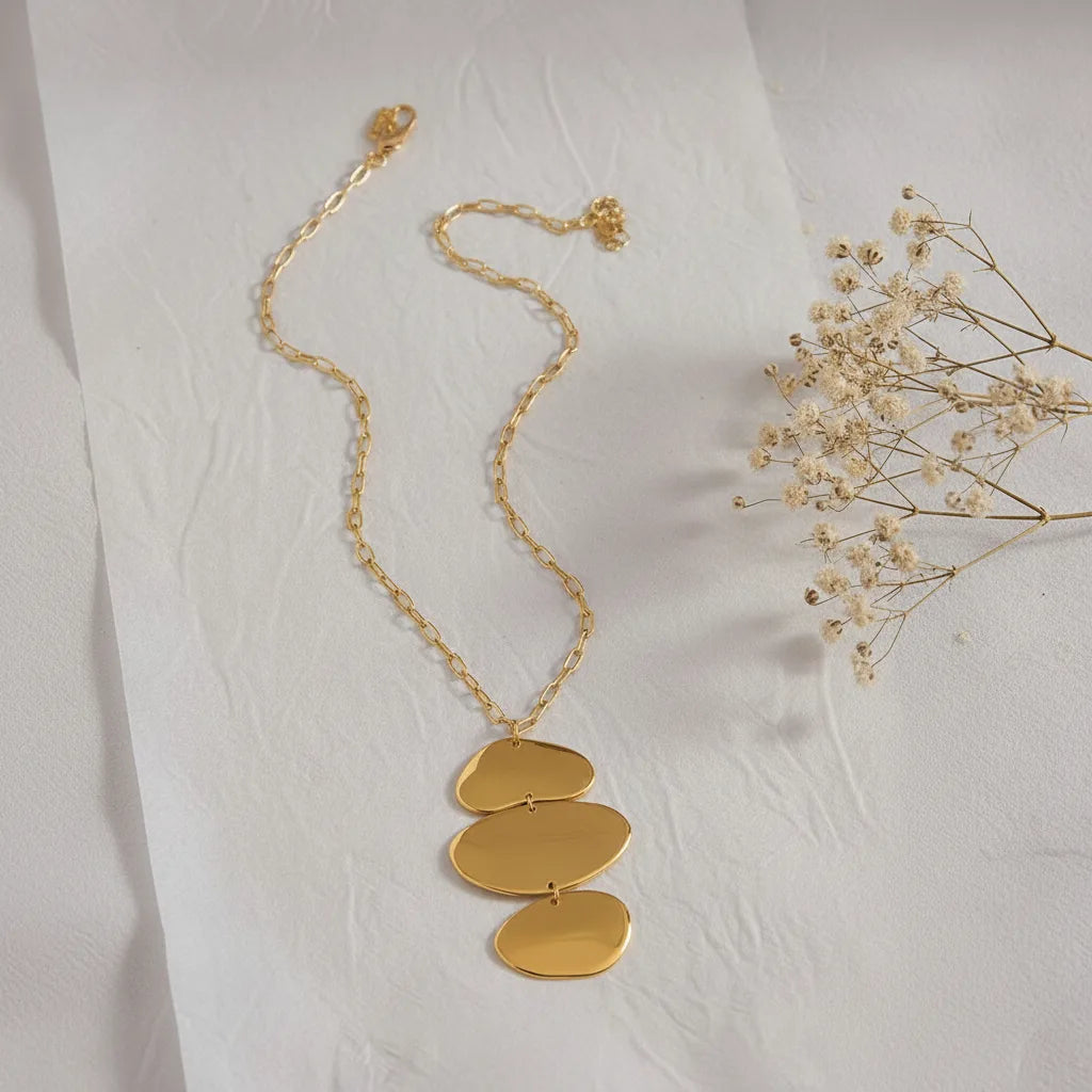 An artistic flat lay of The Thalia Necklace, showing the full length of the adjustable chain and the mirror-like finish of the three-tiered pendant.