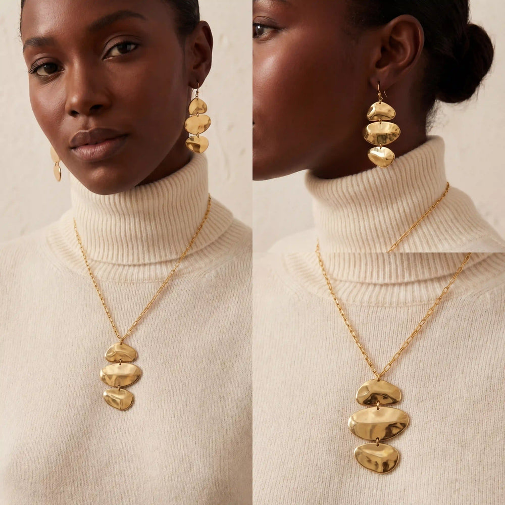 Model with dark skin wearing sculptural gold necklace with white shirt modern style.