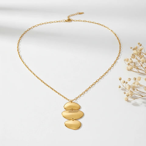 A detailed studio shot of The Thalia Necklace by Luminova, showcasing its sculptural, cascading pendant of three polished gold discs on a delicate chain.