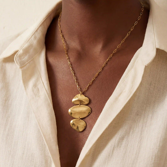 Close up of woman wearing gold Thalia necklace with organic stacked pebble pendant.