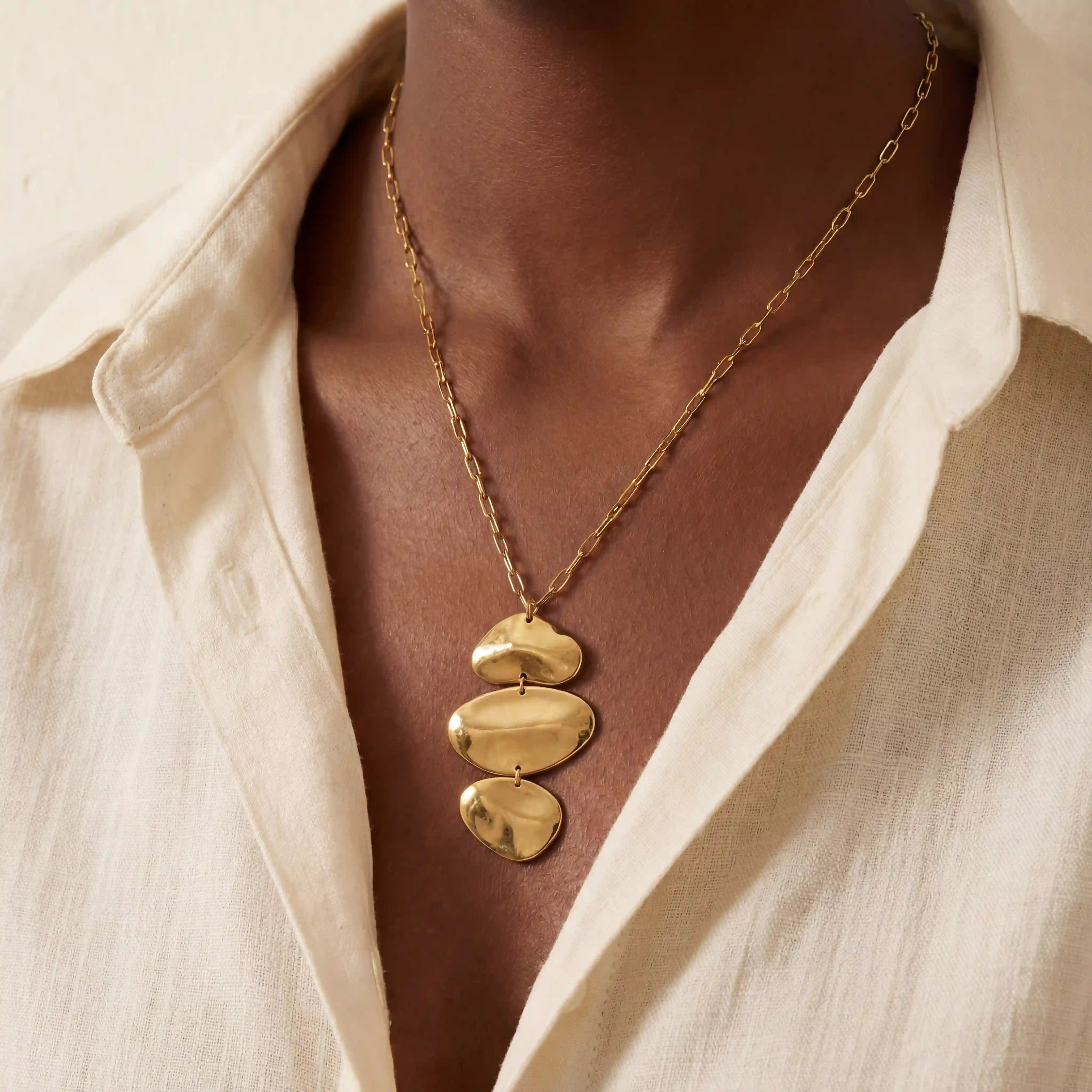 Close up of woman wearing gold Thalia necklace with organic stacked pebble pendant. Main image