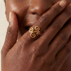 Close up of woman with dark skin wearing gold spiral ring on ring finger laughing.
