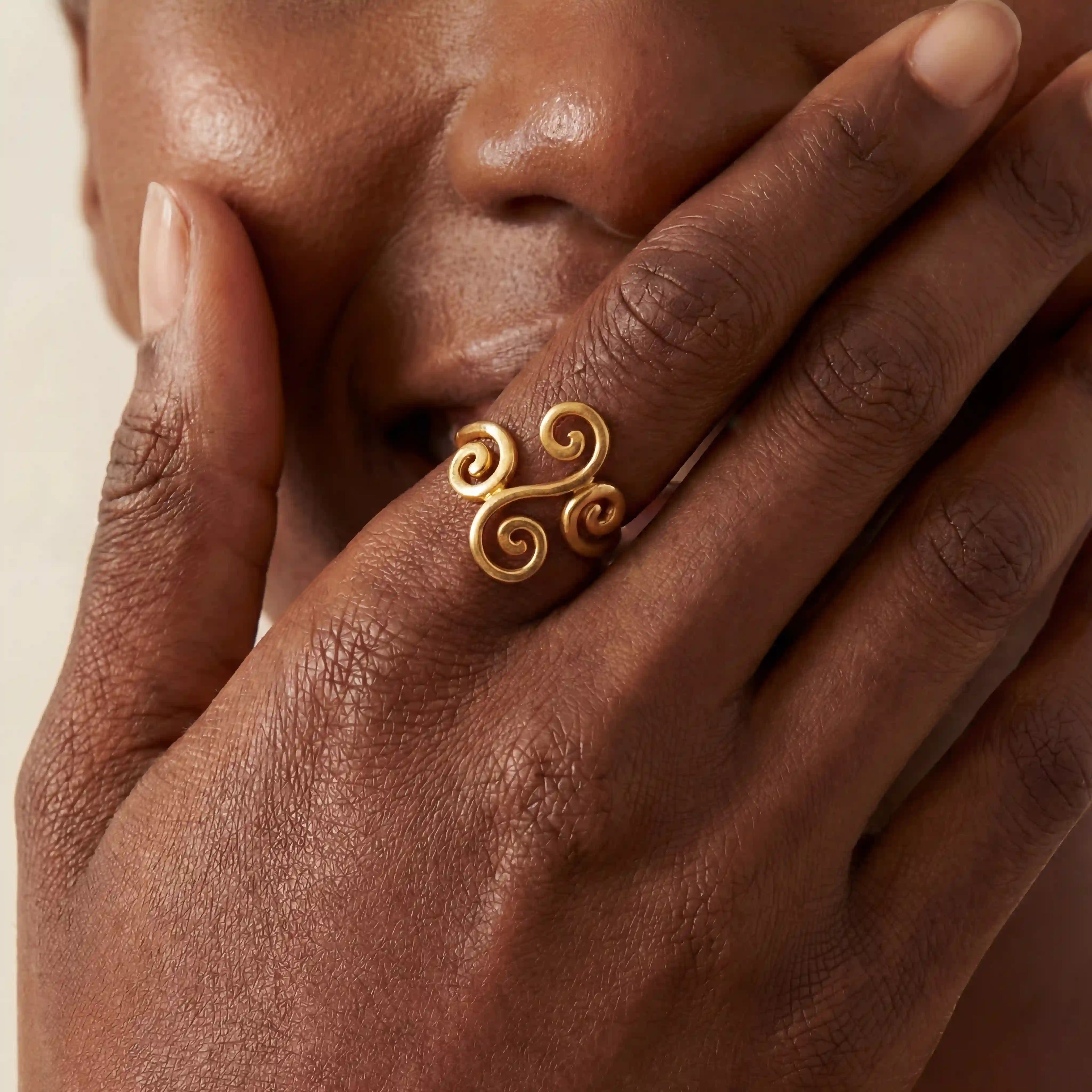Close up of woman with dark skin wearing gold spiral ring on ring finger laughing.