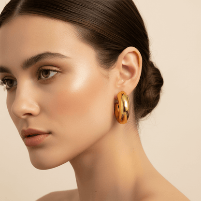 An extreme close-up on a model's earlobe, showing the scale and comfortable fit of the chunky C-shape gold Cloud Hoop. The earring's high-polish finish gleams against her skin.