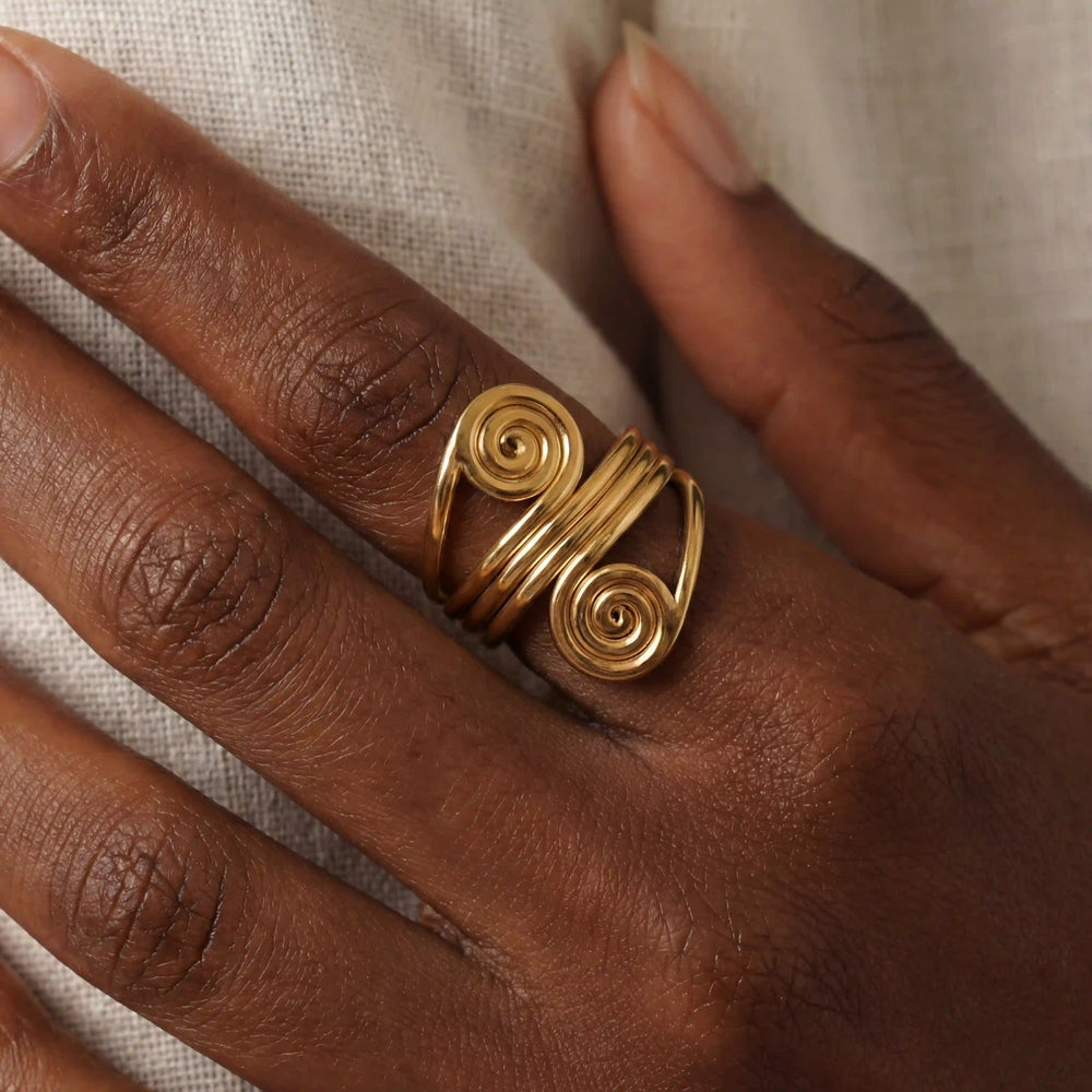 Close up of dark skin model wearing gold spiral statement ring ancient greek style.