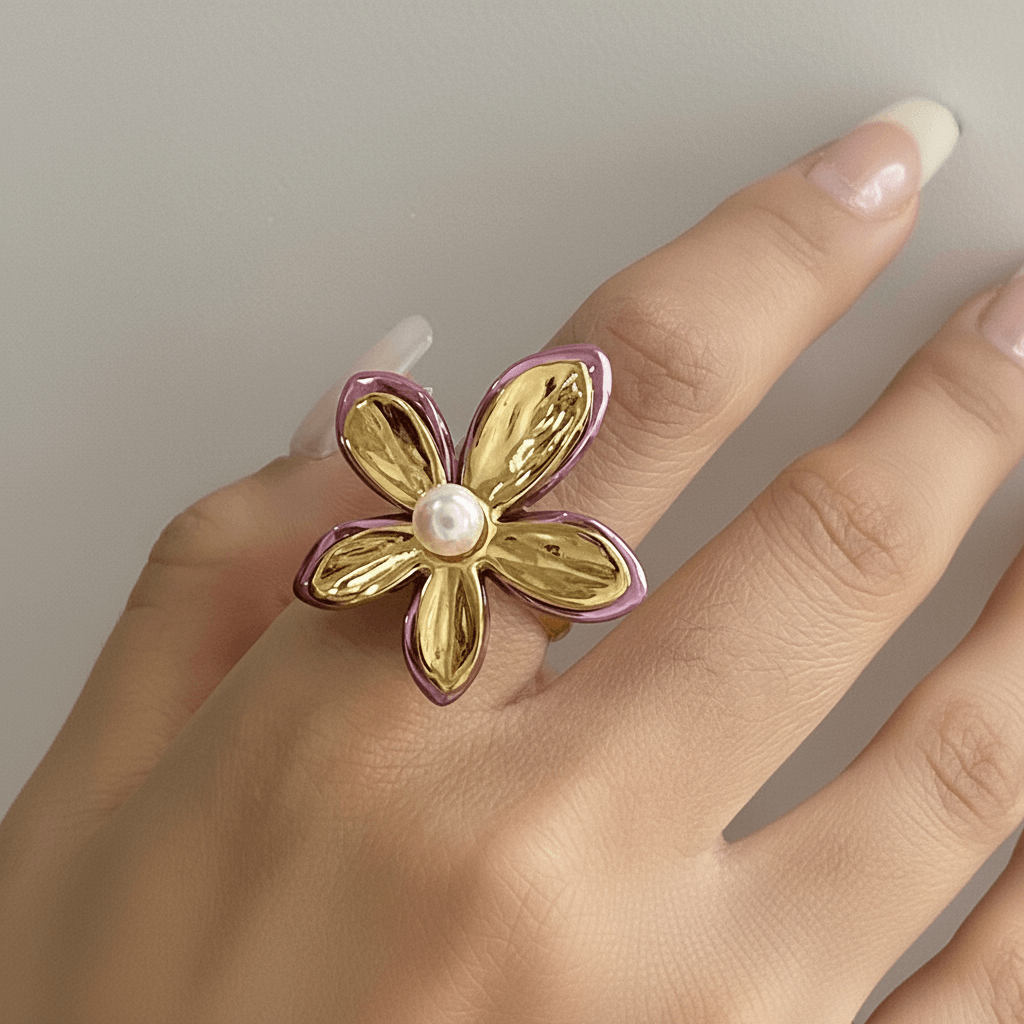 A model's hand with a neutral manicure, showcasing The Orchid Ring worn on her middle finger. The ring's large, sculptural flower design makes a bold and artistic statement.