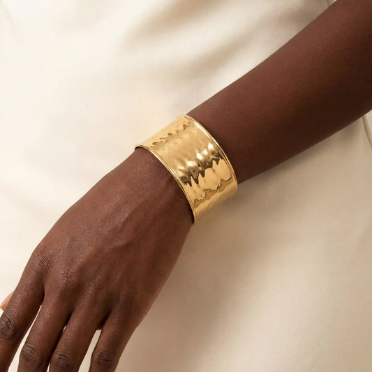 Close up of woman with dark skin wearing wide hammered gold cuff bracelet statement jewelry.