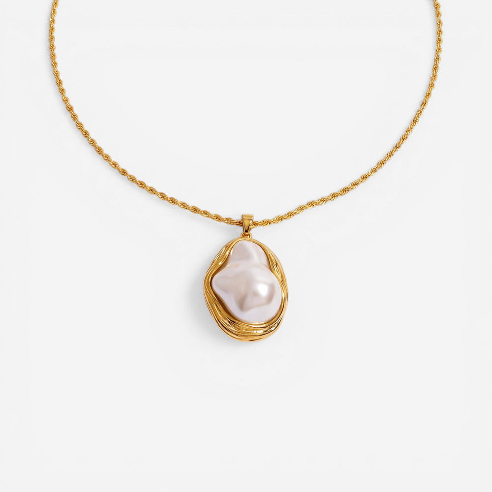 A detailed studio shot of The Theia Necklace by Luminova, showcasing the unique baroque pearl in its sculptural gold pendant on a rope chain, styled with dried flowers.