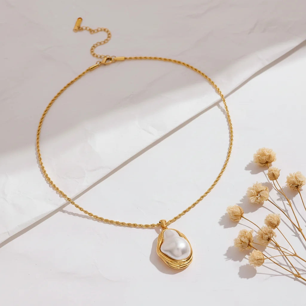 A detailed studio shot of The Theia Necklace by Luminova, showcasing the unique baroque pearl in its sculptural gold pendant on a rope chain, styled with dried flowers.