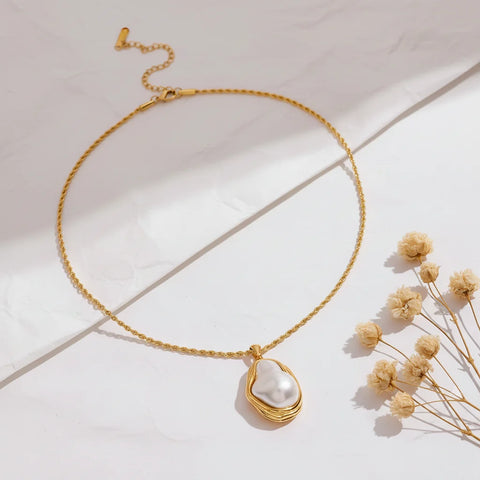 A detailed studio shot of The Theia Necklace by Luminova, showcasing the unique baroque pearl in its sculptural gold pendant on a rope chain, styled with dried flowers.