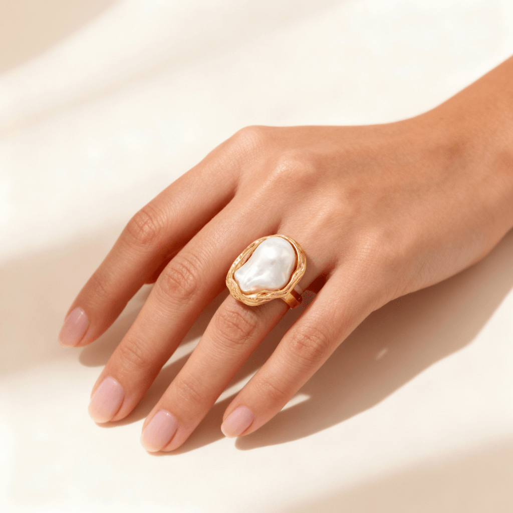 A woman's hand wearing The Theia adjustable baroque pearl ring on her index finger, showcasing its bold scale and comfortable fit against the skin.