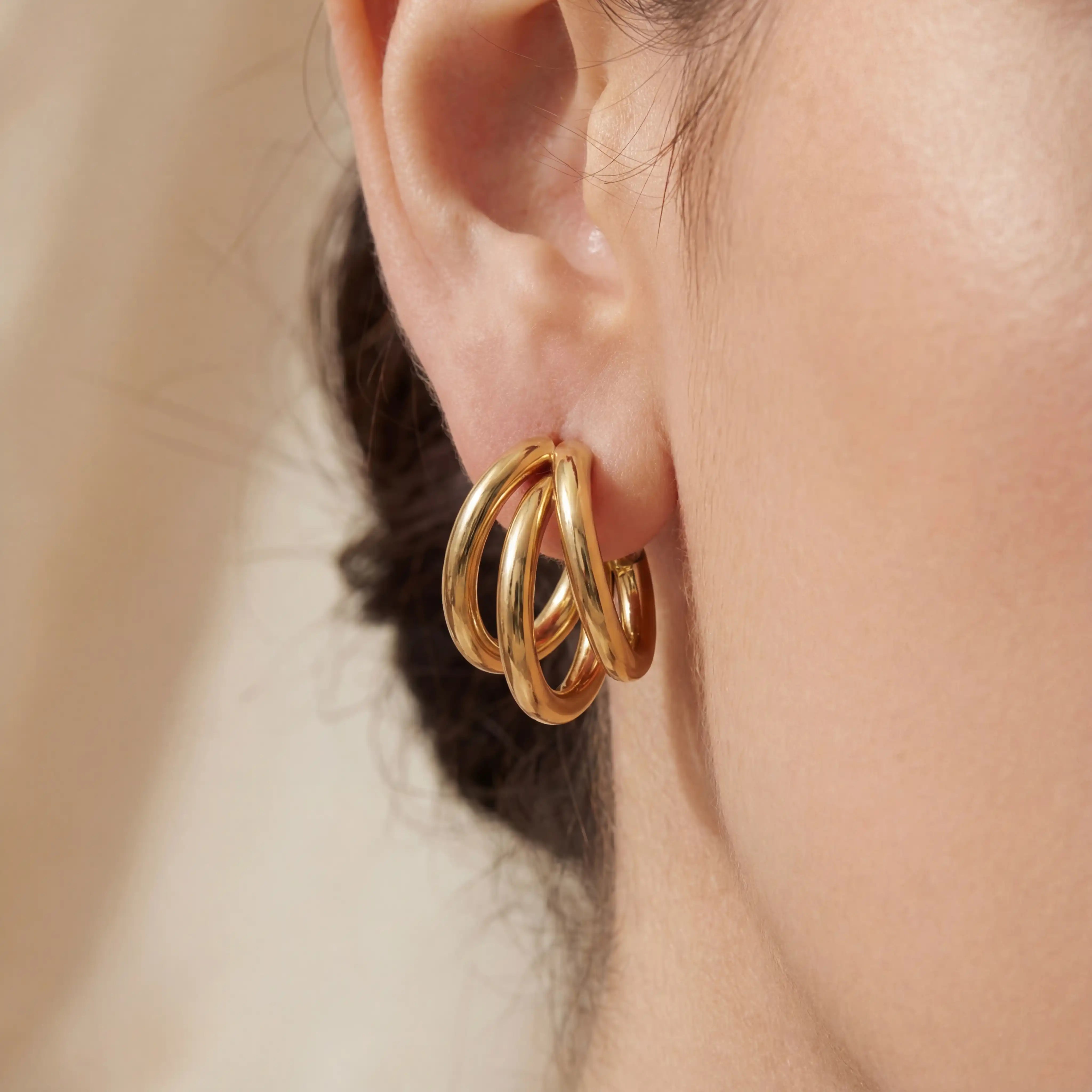 Close up of woman wearing gold triple layer illusion hoop earrings chunky stacked look.