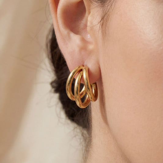 Close up of woman wearing gold triple layer illusion hoop earrings chunky stacked look.