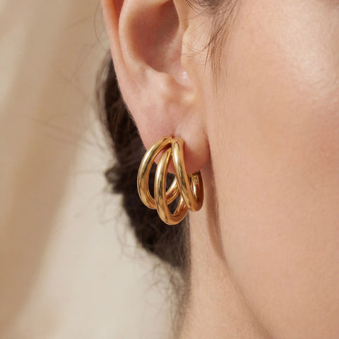 Close up of woman wearing gold triple layer illusion hoop earrings chunky stacked look.