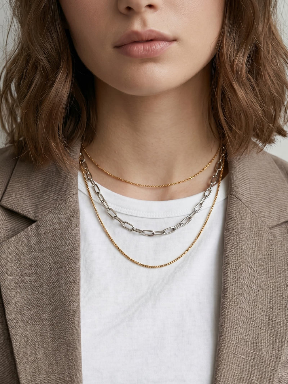 Two-tone layered chain necklace worn with beige blazer and white tank top