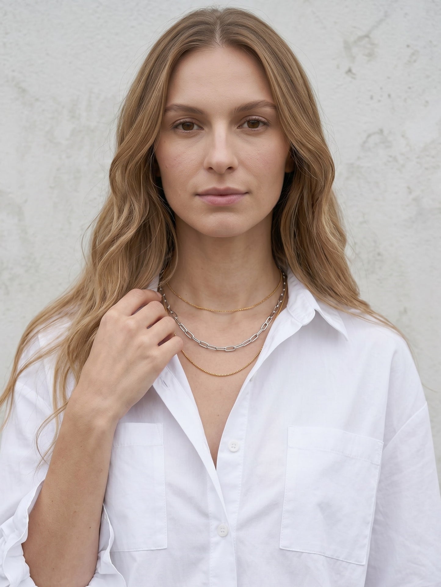 Model wearing mixed metal layered necklace with white button-up shirt