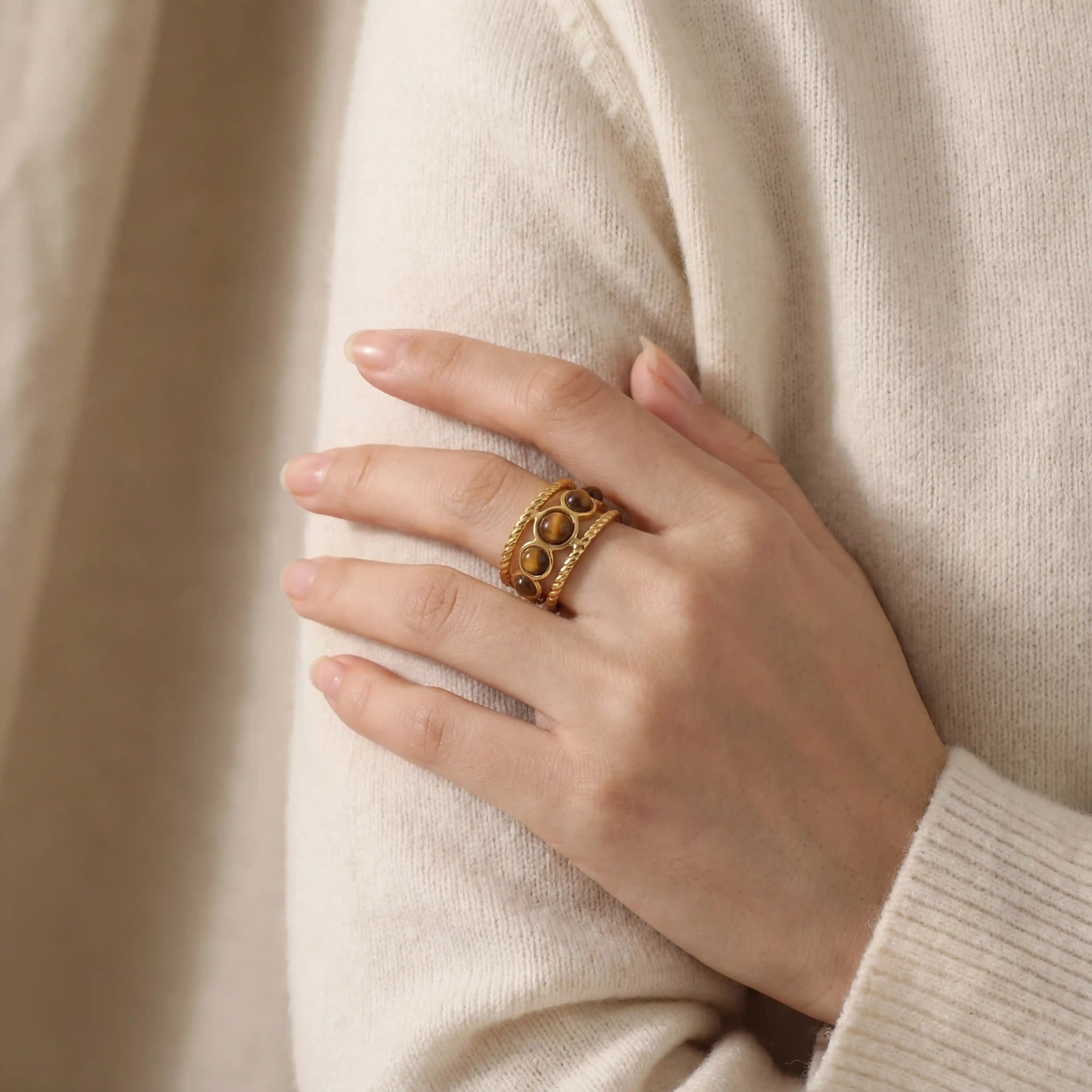 Close up of woman wearing braided gold tiger's eye ring with beige sweater fall fashion.