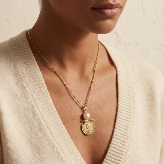Close up of vintage pearl coin necklace with figaro chain on woman wearing cream sweater.