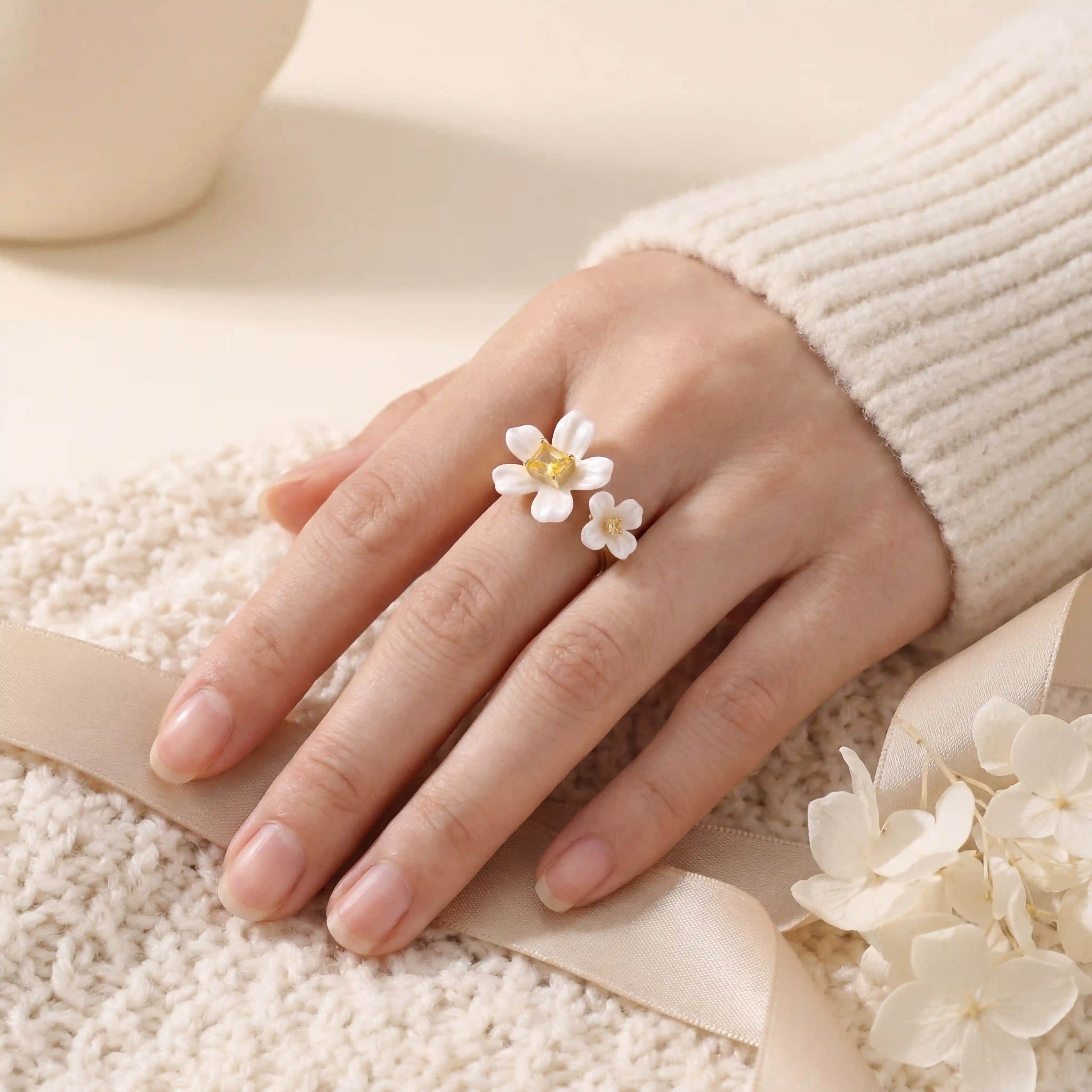 Close up of woman wearing white enamel floral ring with yellow crystal center soft romantic style. Main image