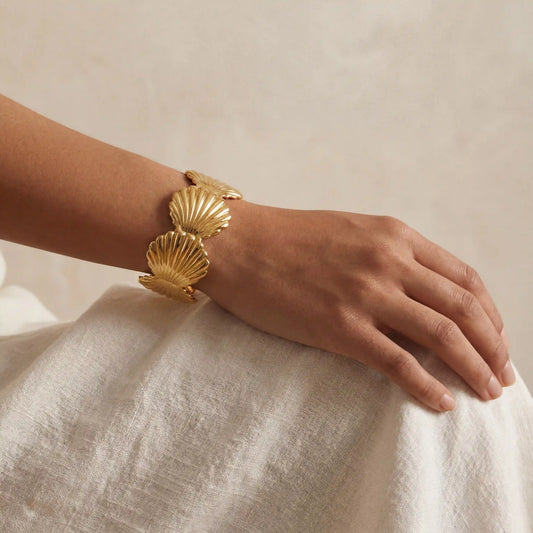 Woman wearing gold scallop shell bangle with white linen dress vacation style.