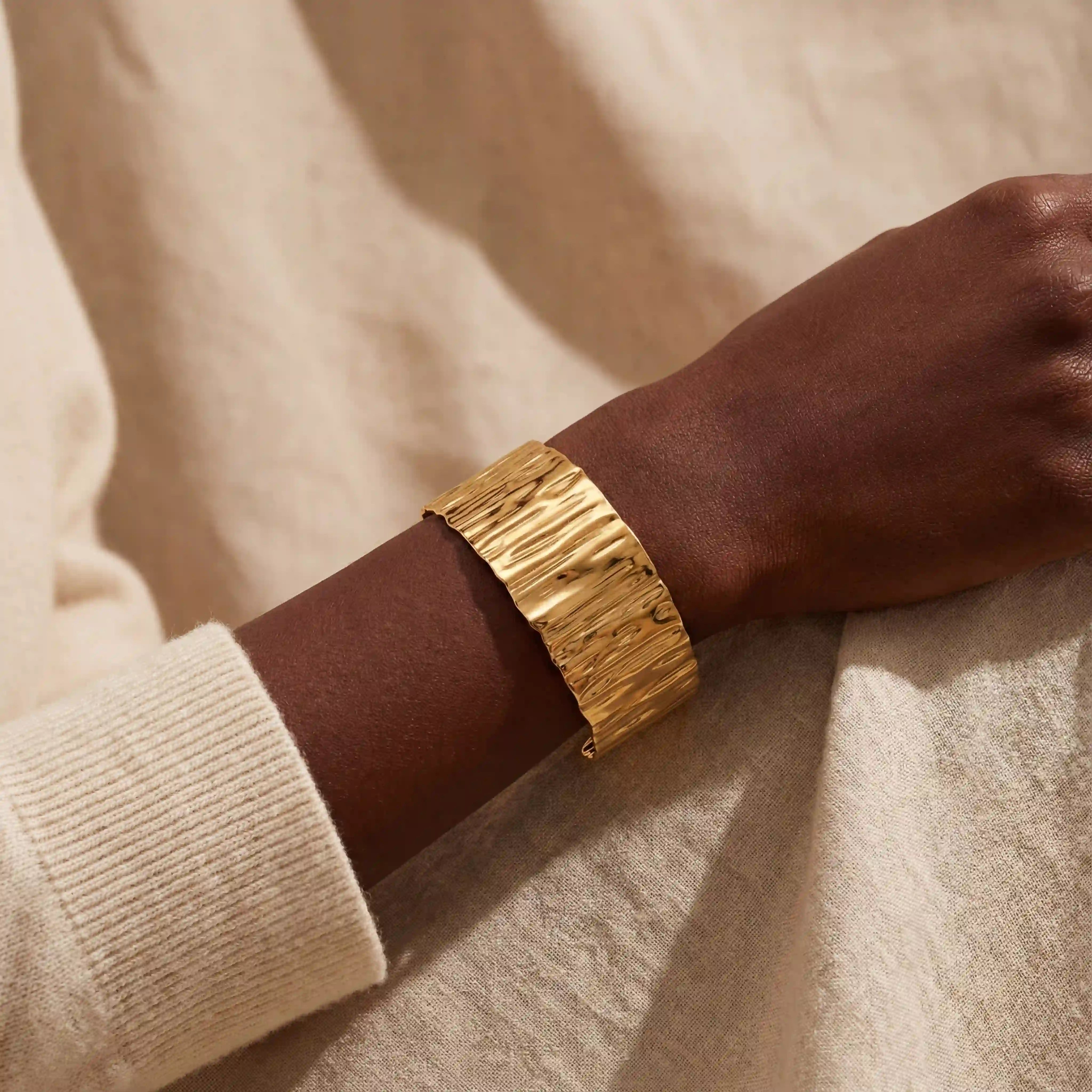 Dark skin model wearing wide liquid gold textured cuff bracelet vintage style.