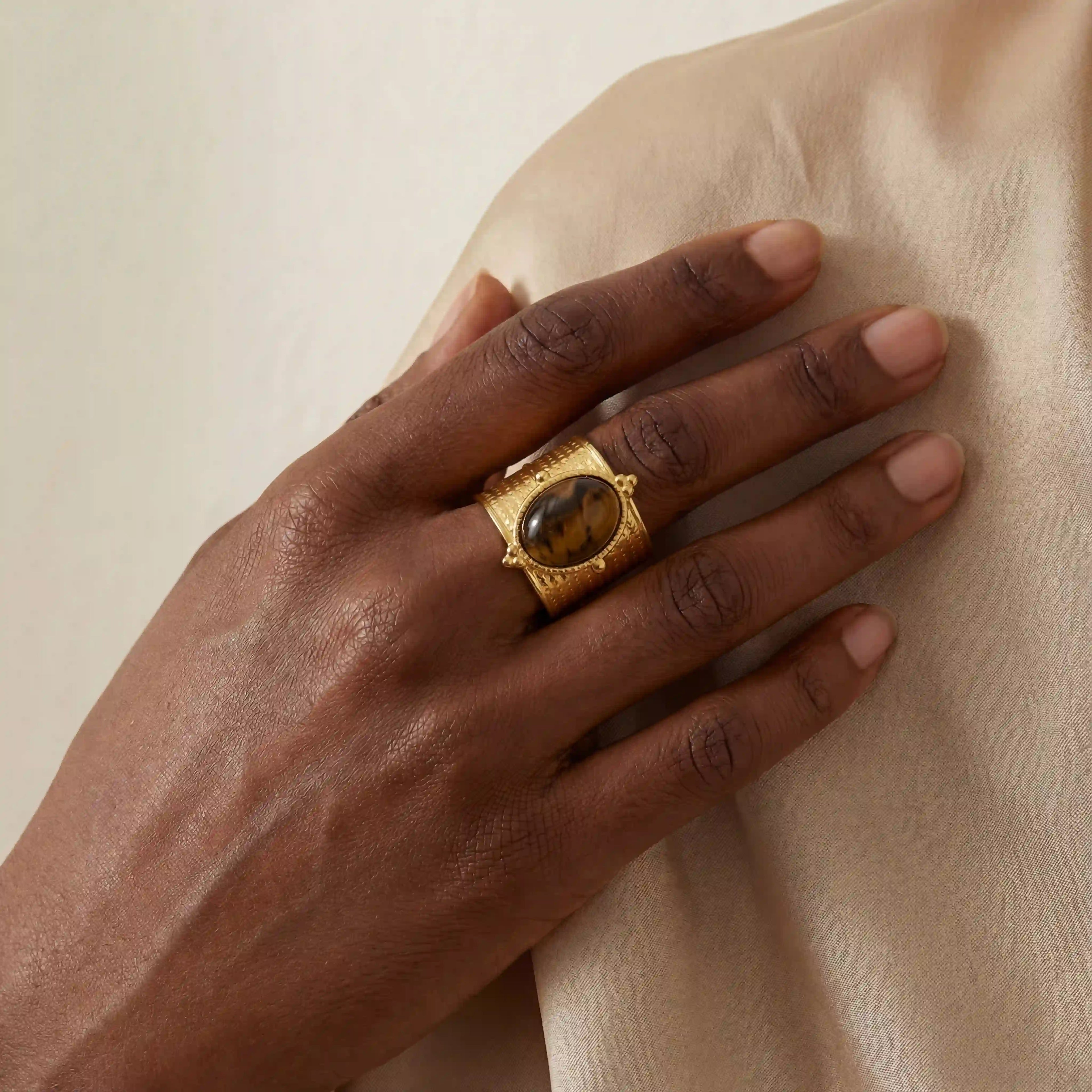 Dark skin model wearing bold vintage tiger's eye cigar band ring on silk background.