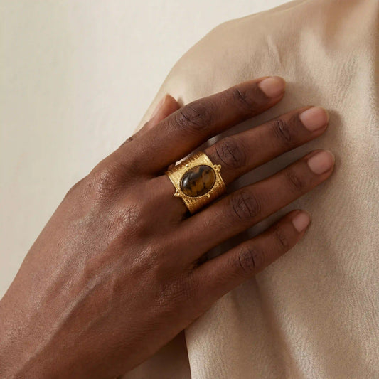 Dark skin model wearing bold vintage tiger's eye cigar band ring on silk background.