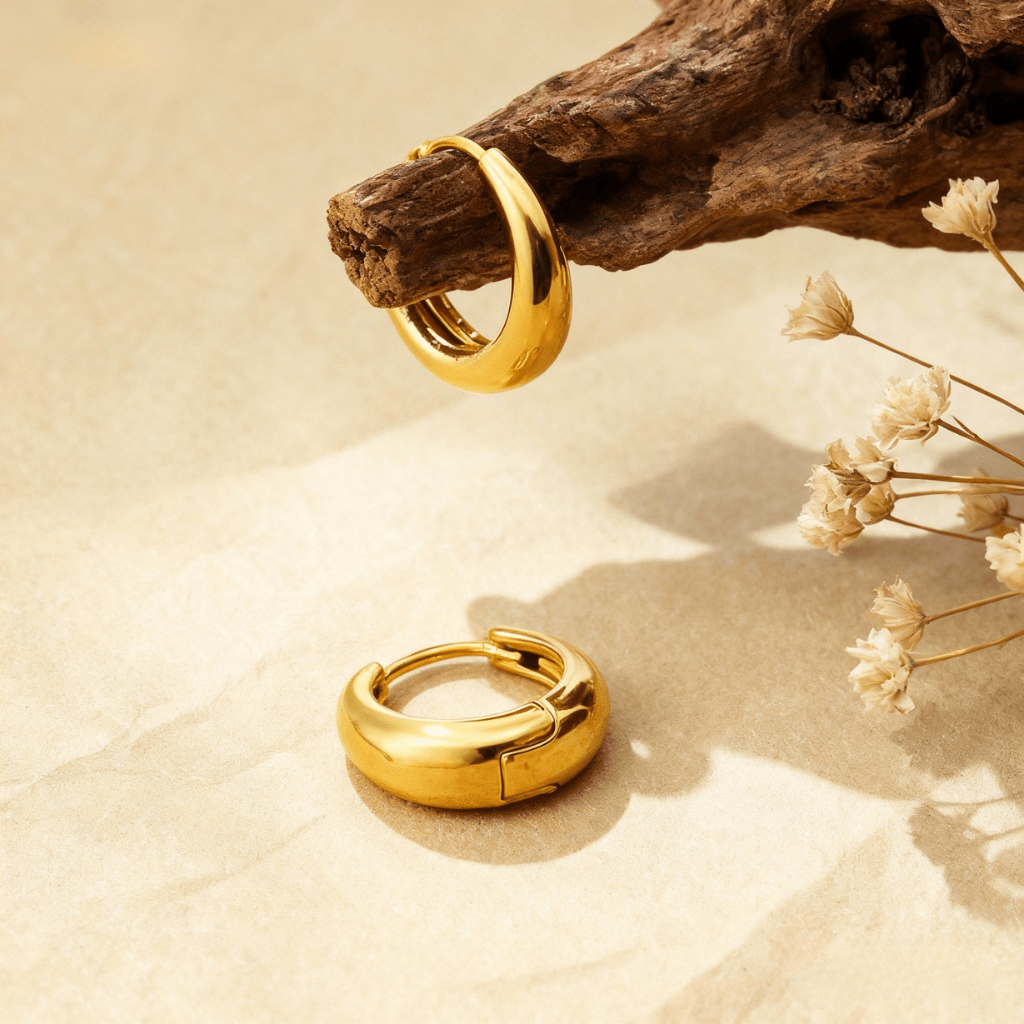 A detailed close-up of a pair of the medium-sized gold Capsule Hoops, showcasing their smooth, rounded surface, high-polish finish, and seamless design on a neutral background.