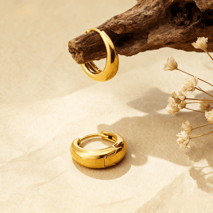 A detailed close-up of a pair of the medium-sized gold Capsule Hoops, showcasing their smooth, rounded surface, high-polish finish, and seamless design on a neutral background.