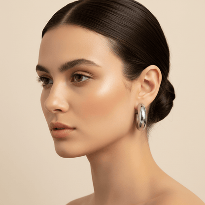 A close-up on a model's neck and jawline, showing her wearing the chunky silver Cloud Hoops paired with a delicate silver necklace, demonstrating how to style the statement earrings.