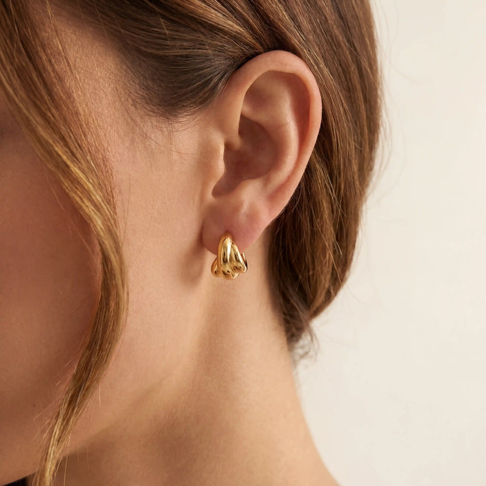 Close up of Amelie gold croissant hoop earrings on ear, small twisted dome hoops for everyday wear, waterproof hypoallergenic stainless steel jewelry.