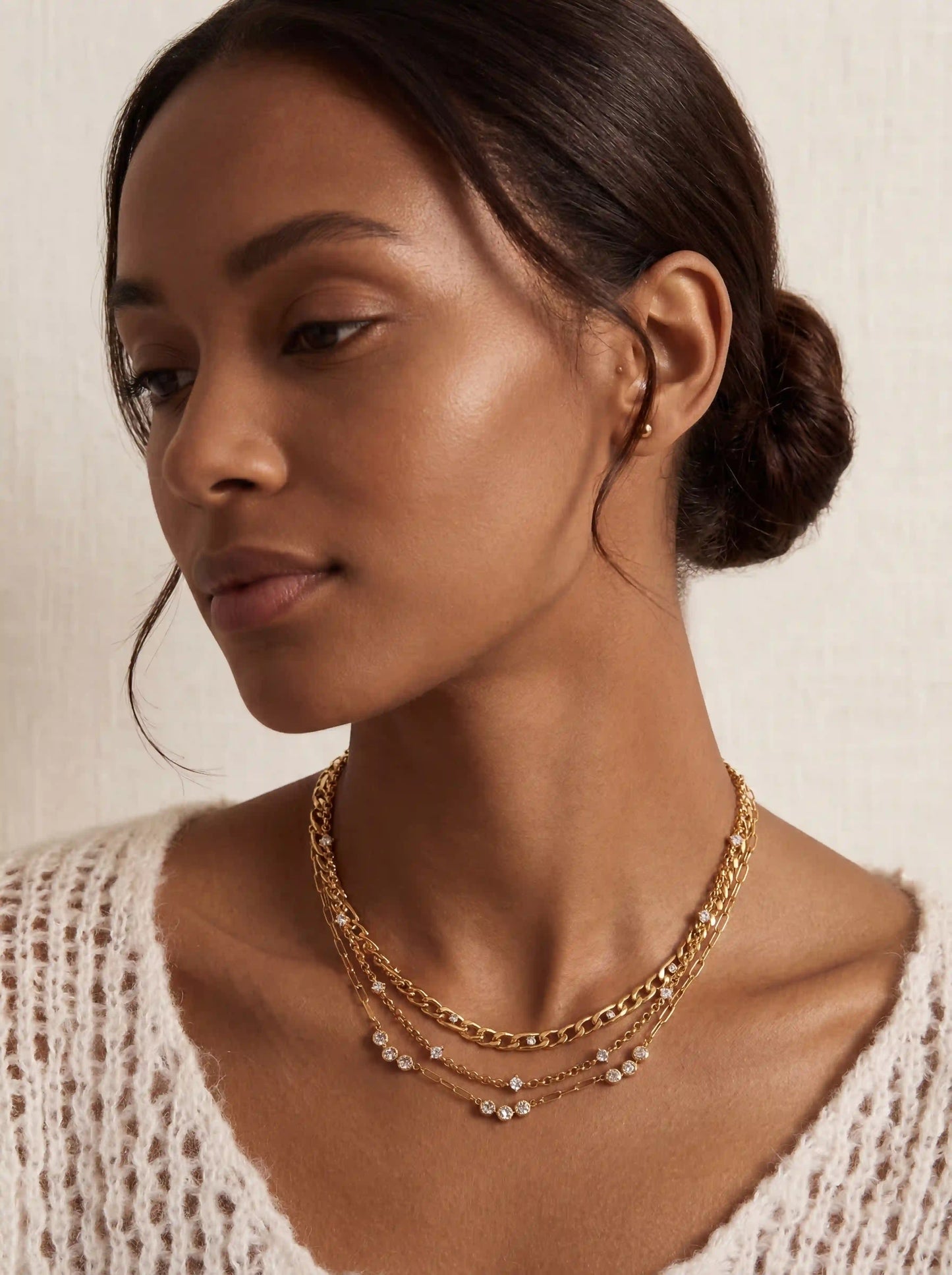 Model with dark skin wearing gold crystal station necklace in a layered necklace stack boho style.