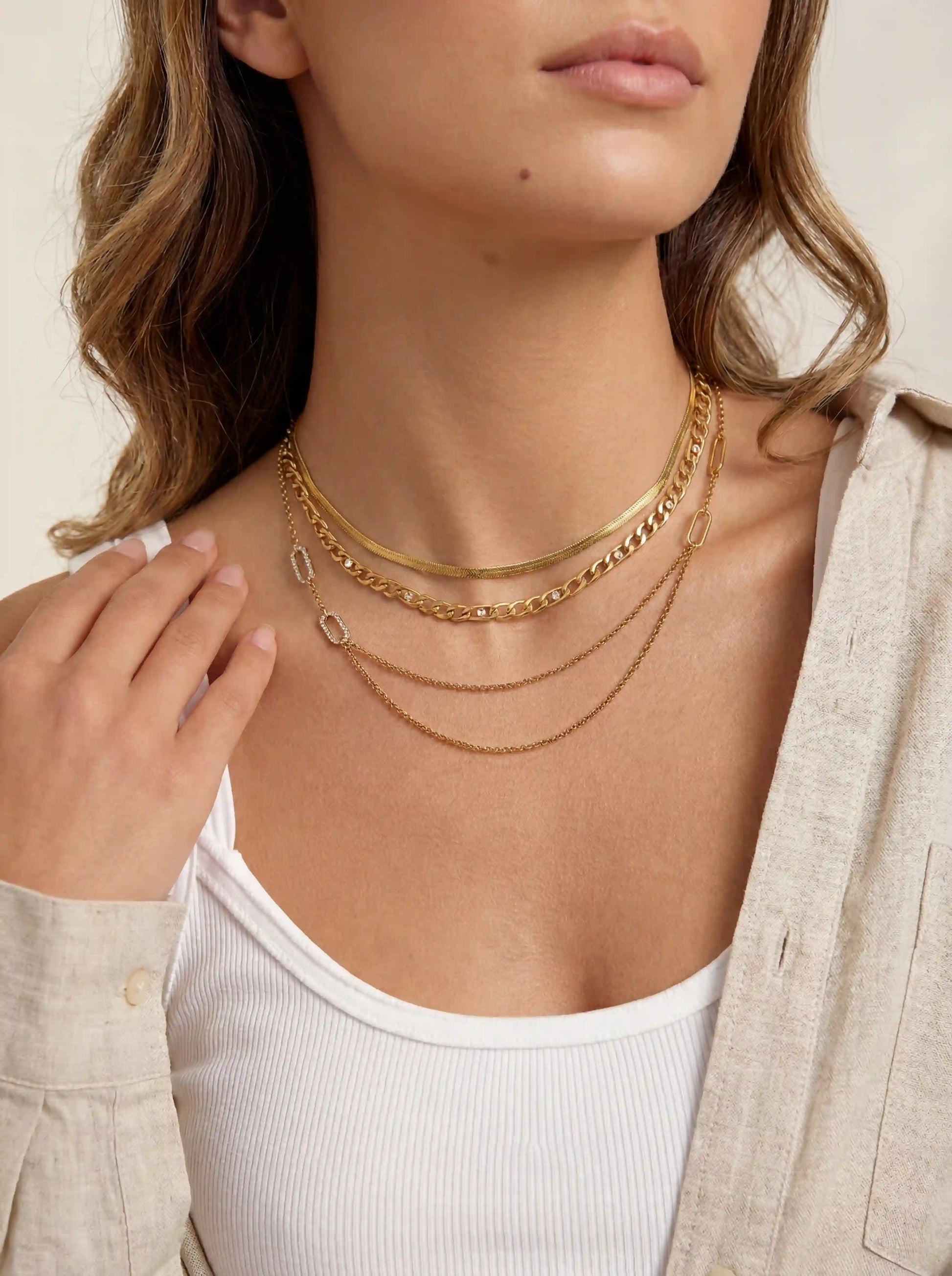 Blonde woman styling gold crystal chain necklace in a chic three layer necklace stack.