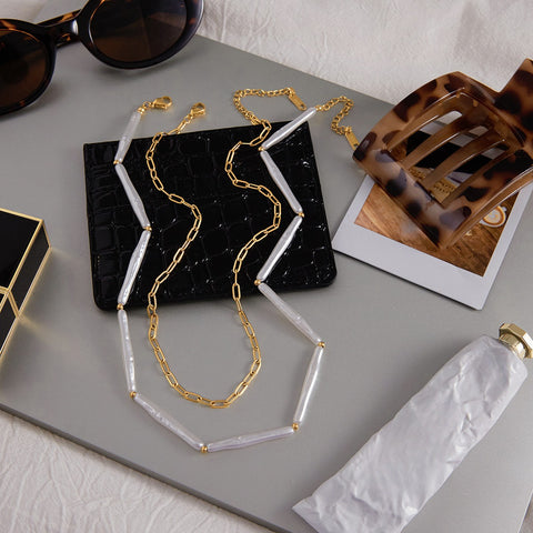 A chic flat lay featuring The Callisto Necklace with sunglasses and a pastry, evoking a sense of Parisian style and a sophisticated brunch look.