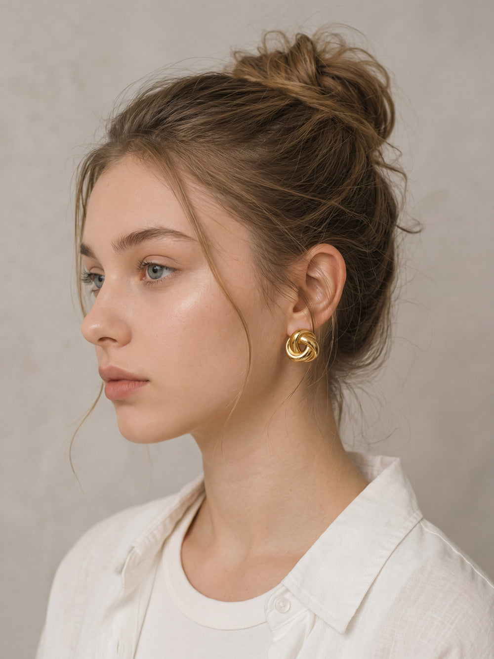 Chunky gold knot stud earrings worn on ear in a close-up side view