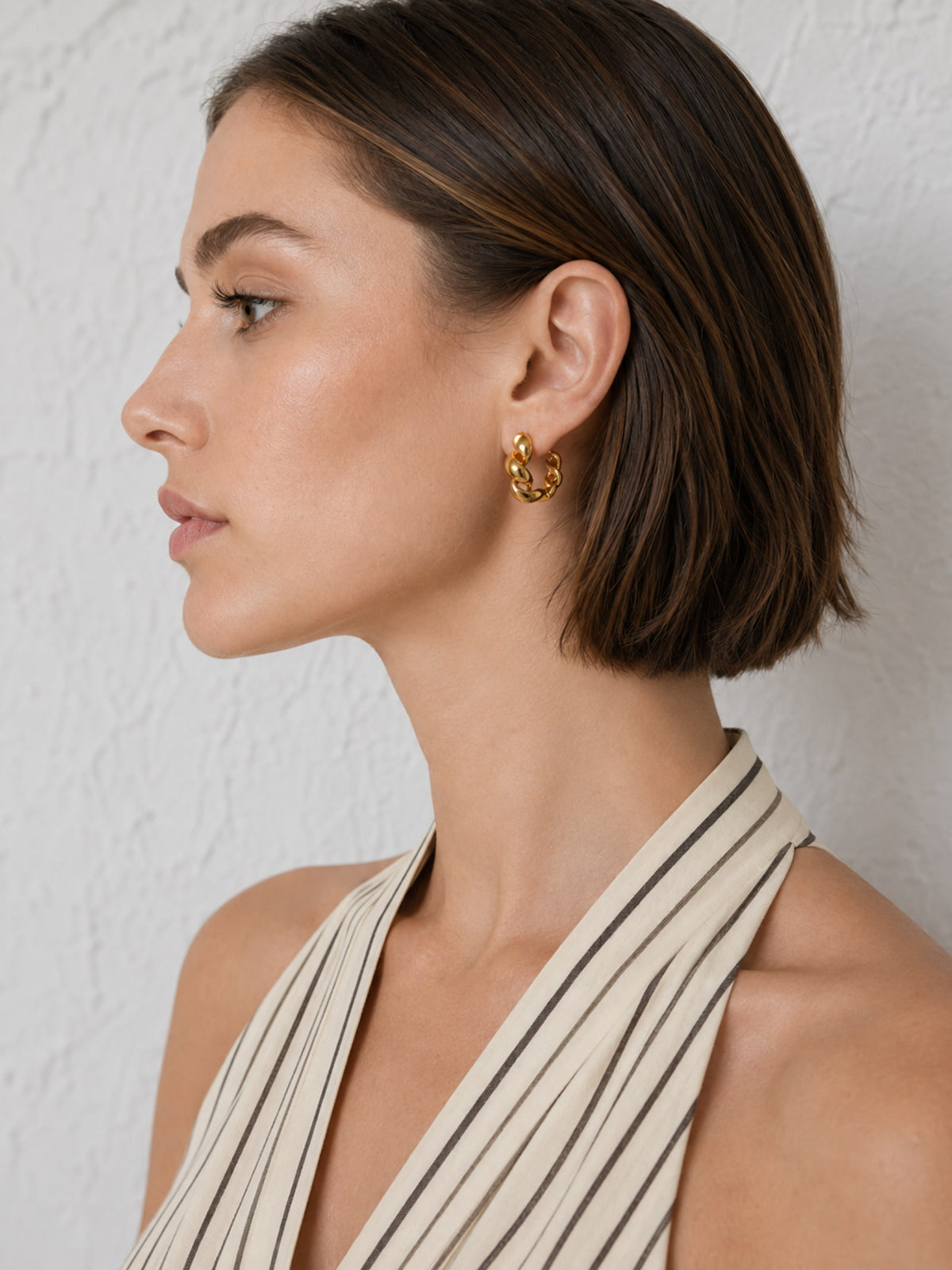 Model close-up wearing compact chunky twisted gold hoop earrings