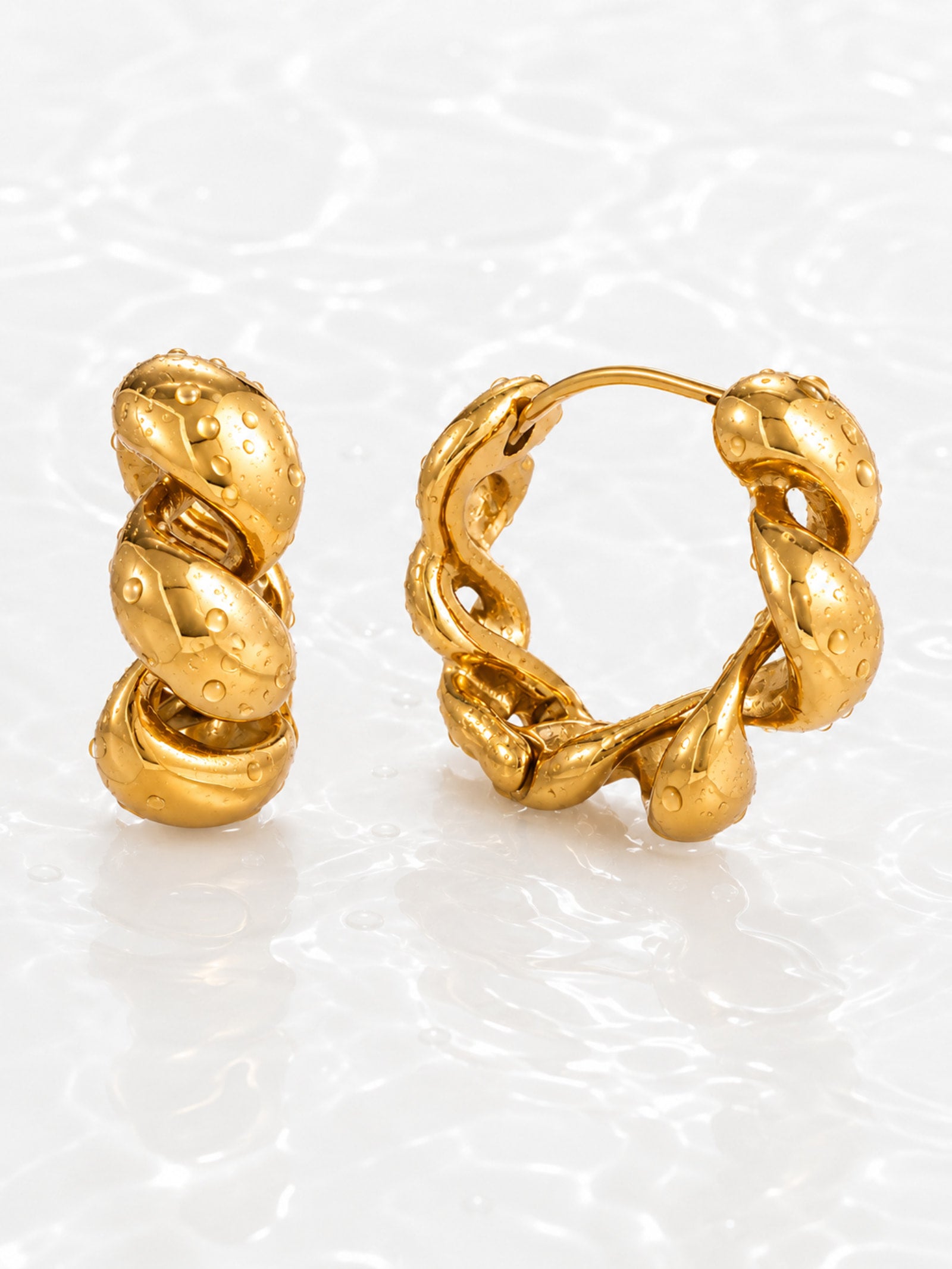Chunky twisted gold hoop earrings with water droplets on white water ripple background